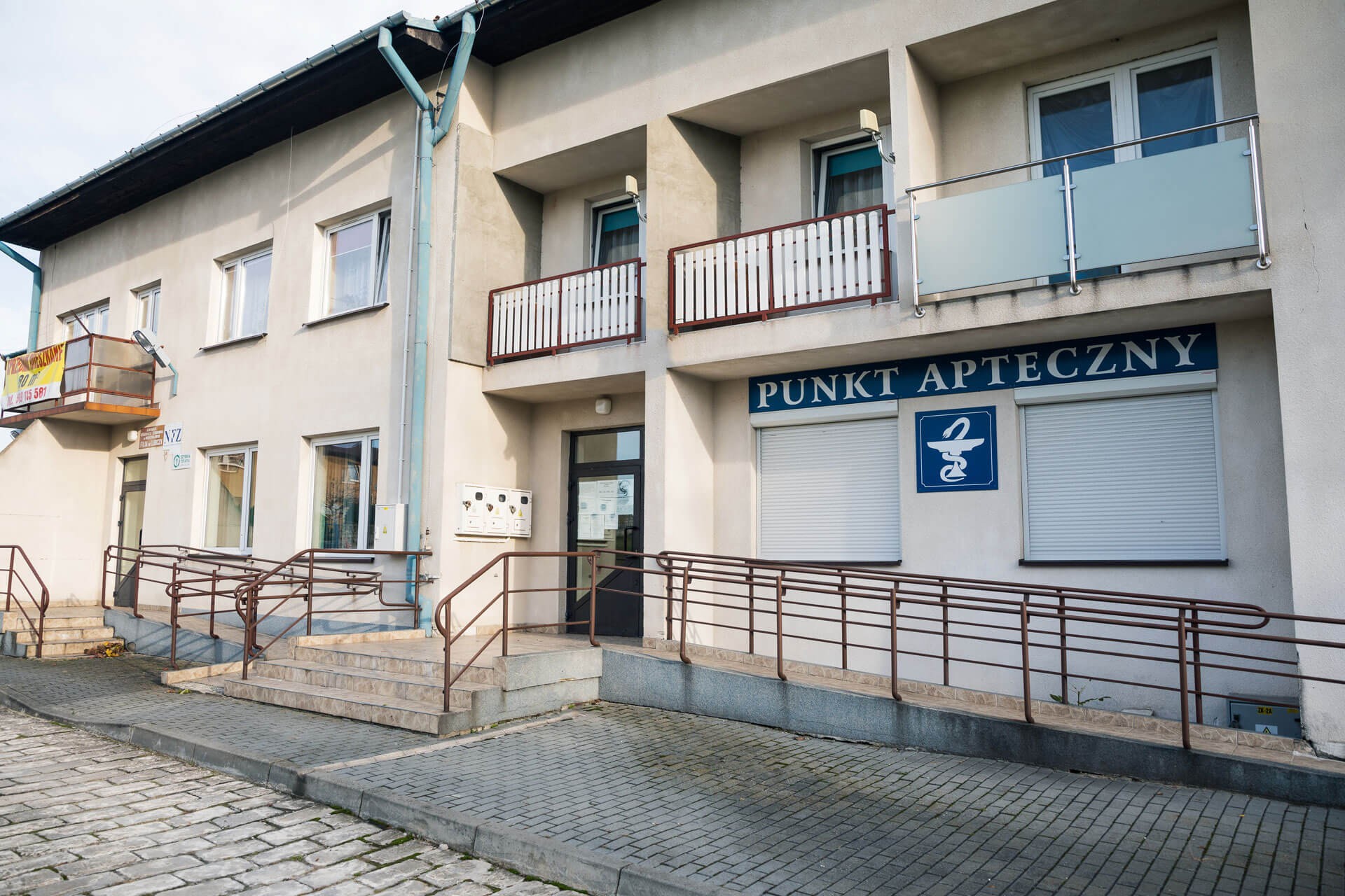 Wejście do budynku Gminnego Ośrodka Zdrowia w Wodzisławiu, filia w Lubczy – przed wejściem znajdują się schody oraz podjazd dla wózków.